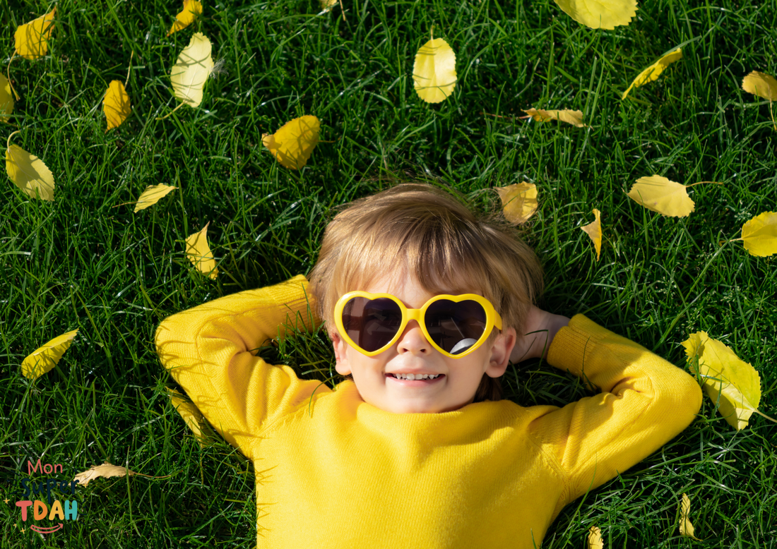 Enfant allongé dans l'herbe, souriant, portant des lunettes en forme de cœur