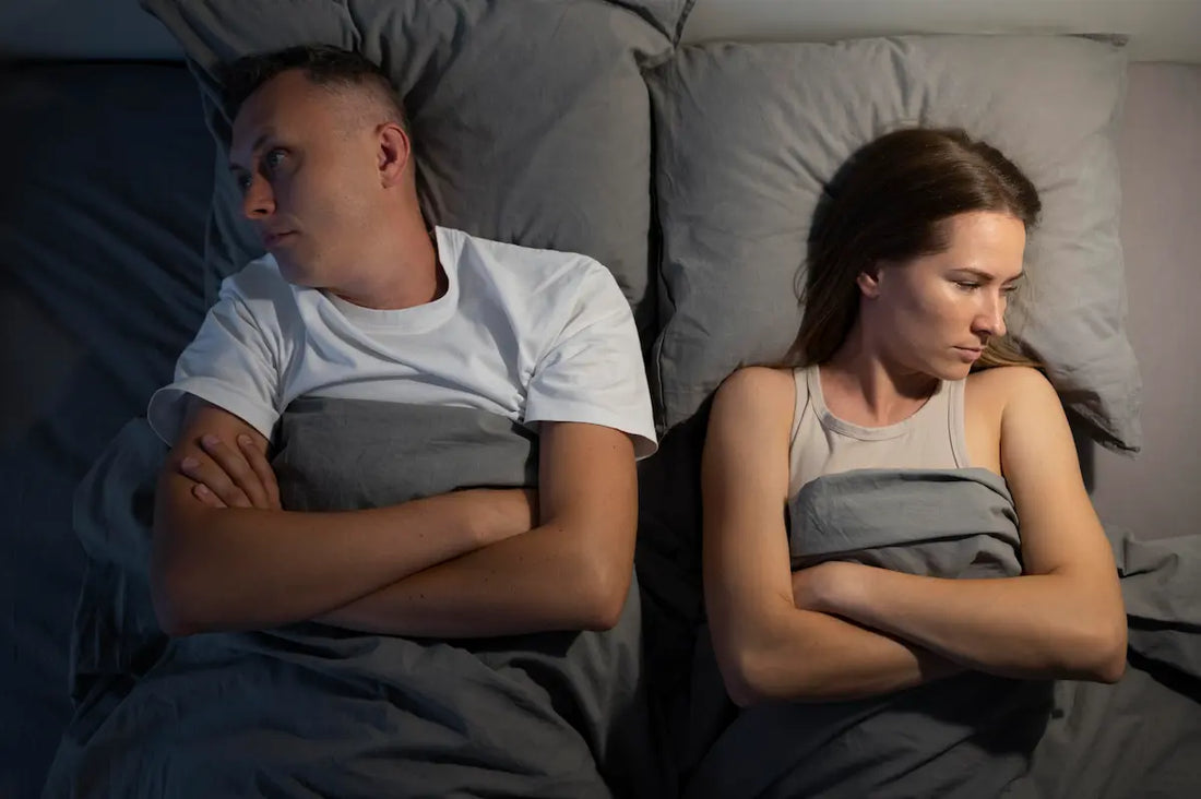 Couple allongé dos à dos dans un lit, bras croisés, tension dans la relation