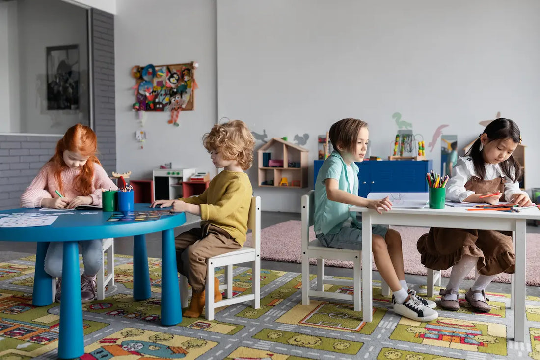 Quatre enfants assis à des tables colorées en classe, en train de dessiner et travailler