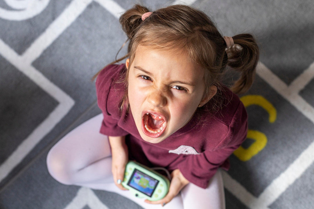 Petite fille en pleine crise de colère, vue de dessus, tenant une console de jeu